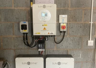 sunsynk inverter and two batteries on a block wall