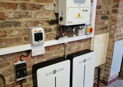 sunsynk inverter and two batteries on a brick wall