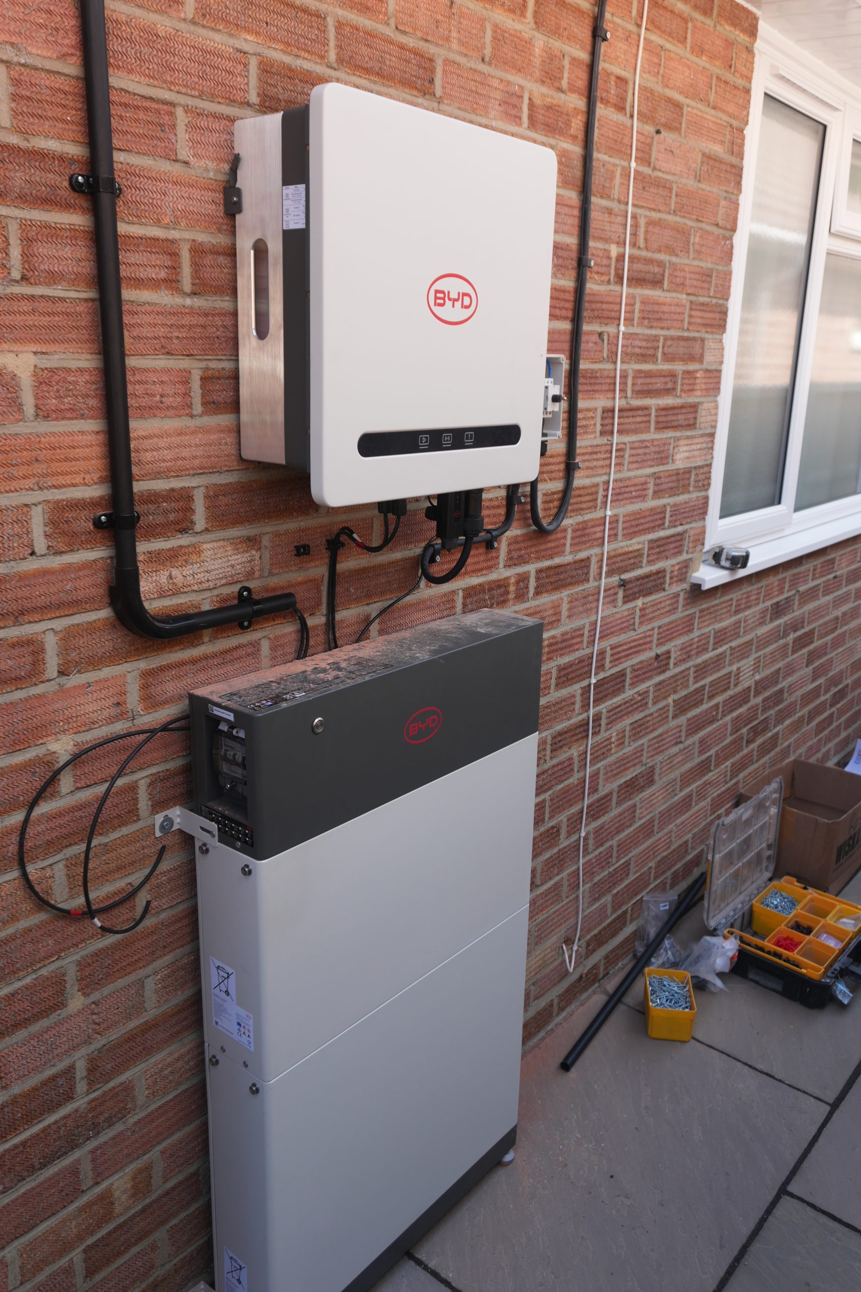 Close-up of the BYD Power-Box SH4.6K hybrid inverter with isolator, neatly installed on a brick wall